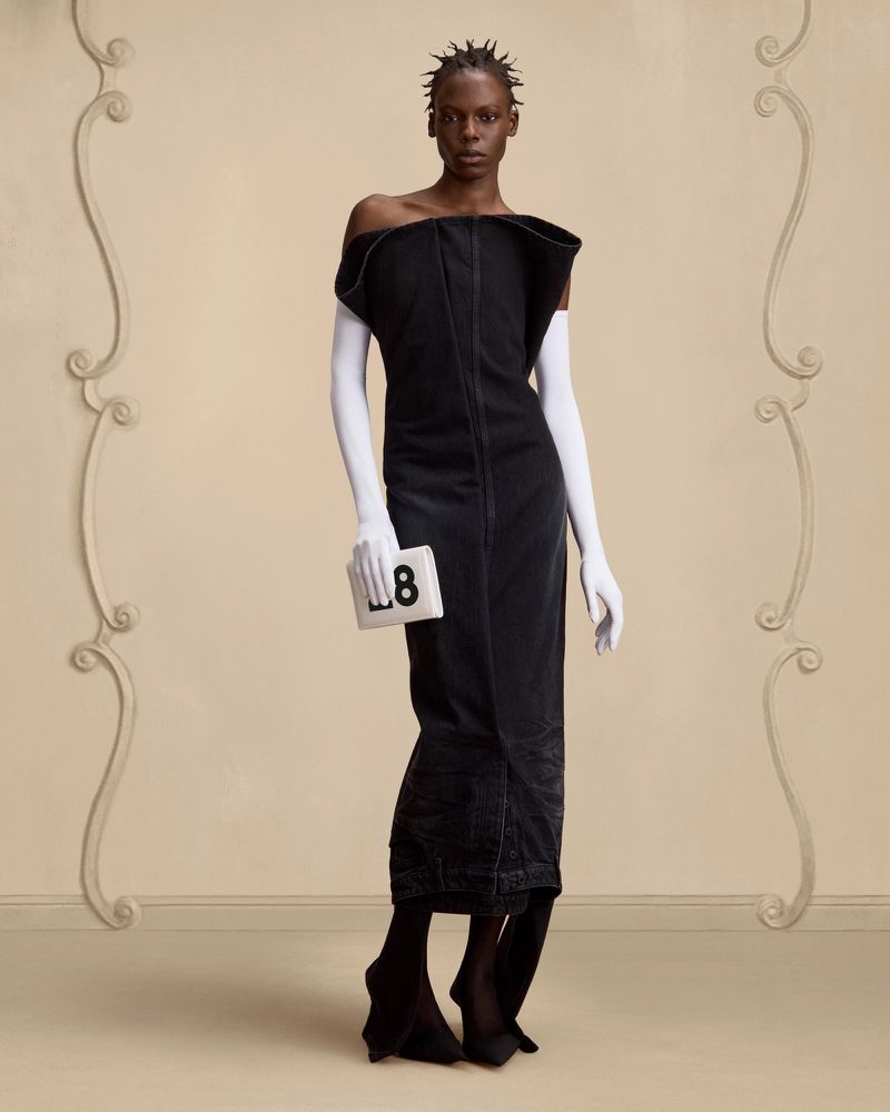 Elegant editorial fashion shot featuring a Black woman in a black dress, white gloves, and statement shoes holding a white card with the number 8.
