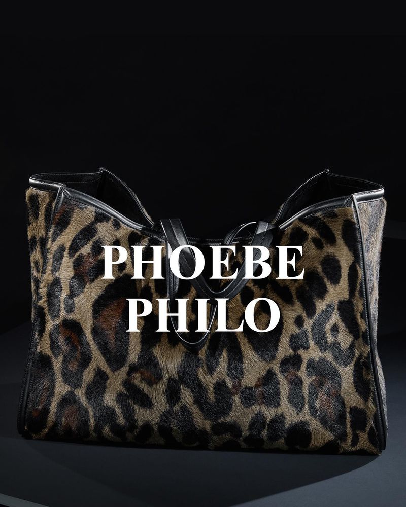 Leopard print handbag with black leather trim and handles against a dark backdrop. Designer Phoebe Philo's name is overlaid on the bag.