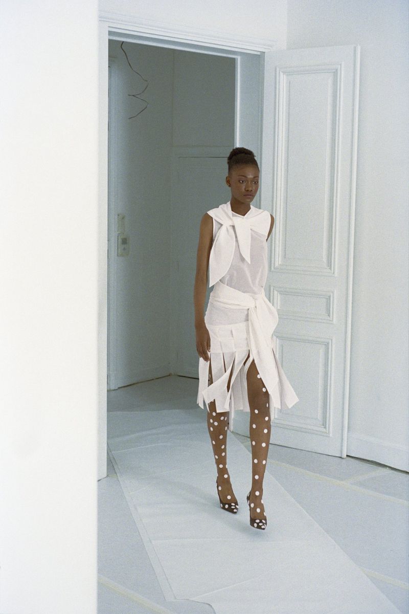Fashion runway: An African American woman in a white outfit with polka dot tights walks through a white doorway during a show.