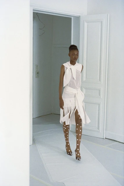 Fashion runway: An African American woman in a white outfit with polka dot tights walks through a white doorway during a show.