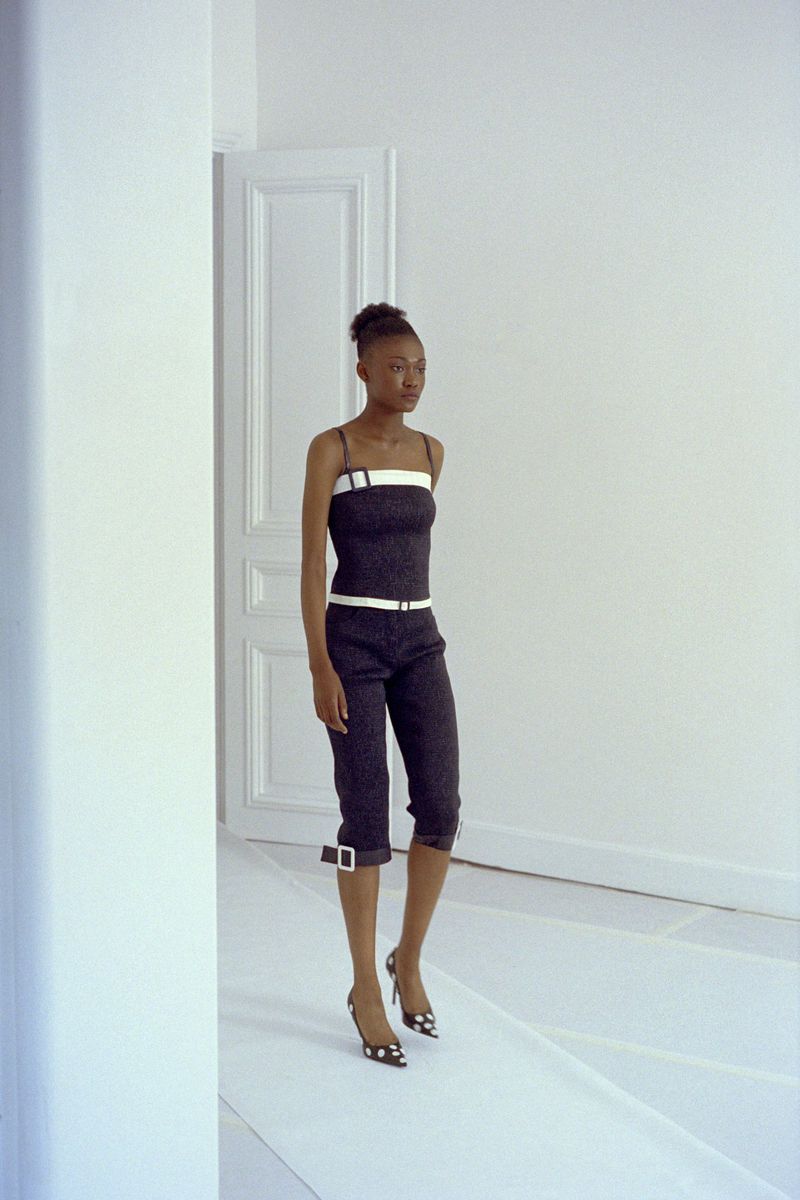 A slender woman with dark skin and her hair up is shown in a fashion pose in a strappy top and capri pants, with a bright white background.