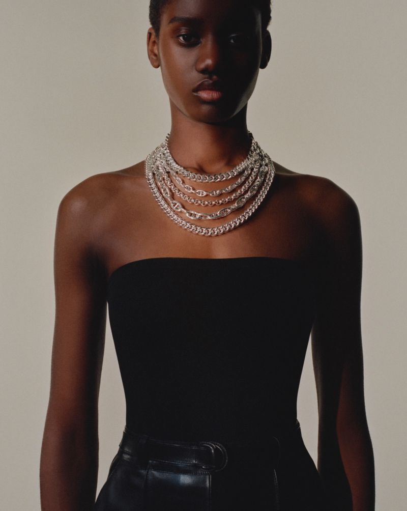 Close-up shot of a Black woman wearing a strapless top and layered chain necklaces in a studio with a neutral background.