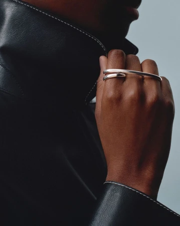 Close-up of an adult with medium skin tone wearing a black leather jacket and a silver ring on the middle and ring fingers.