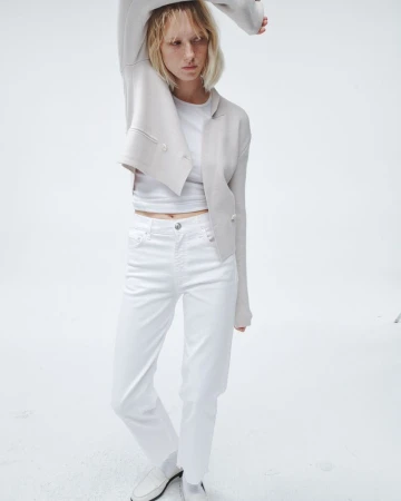 Full-shot of a woman in white jeans and a cream blazer against a white background, creating a clean and minimalist fashion image.