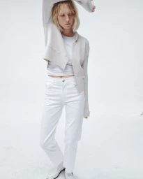 Model posing in a cropped light grey jacket, white top, and white straight-leg denim jeans against a white seamless background.