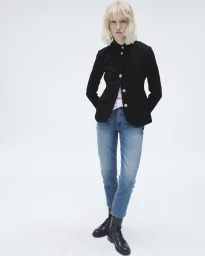 Model with blonde hair wearing a fitted black buttoned jacket, blue jeans, and black lace-up combat boots on a white background.