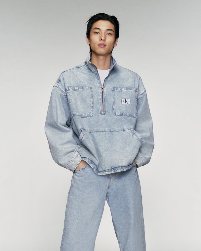 Adult male poses in denim jacket and jeans in a studio shot. The man is dressed in a light-blue denim outfit against a neutral backdrop.