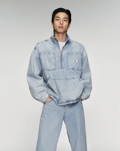 Adult male poses in denim jacket and jeans in a studio shot. The man is dressed in a light-blue denim outfit against a neutral backdrop.