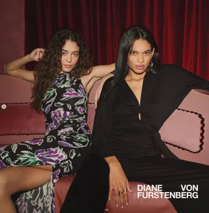 Two female models posing seated together on a pink sofa against deep red curtains for Diane von Furstenberg summer campaign