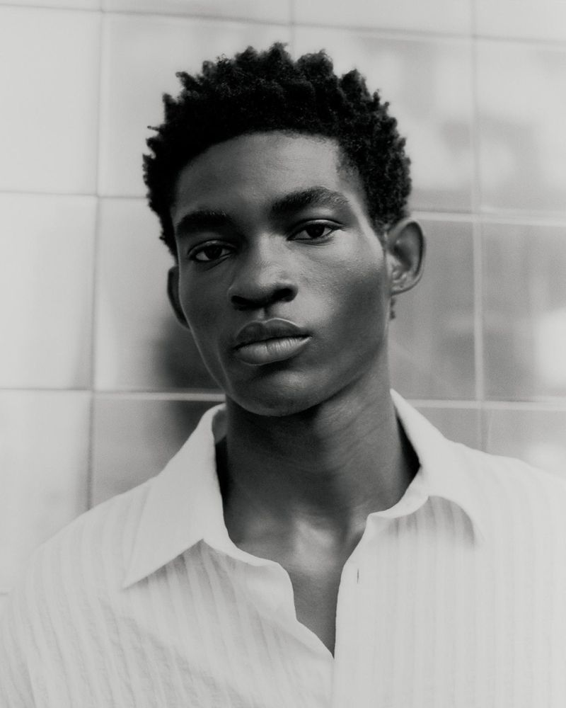 Monochromatic portrait of a dark-skinned male model in a button-down shirt against a tiled backdrop, showcasing a close-up perspective.