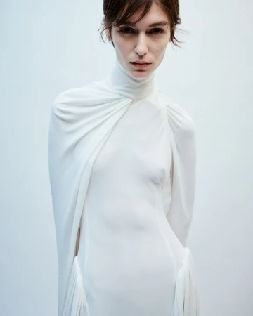 Model wearing a white high-neck draped dress against a light background for 16Arlington AW24 Lookbook