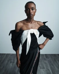 Model Amelie Nsengiyumva wearing an off-the-shoulder black top with a white tied bow detail for Hellessy Resort 25.