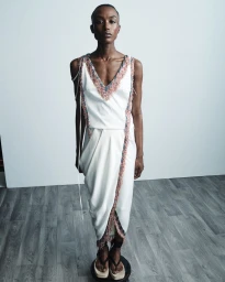 Amelie Nsengiyumva in a white fringe-trimmed draped dress and platform sandals for Hellessy Resort 25.