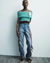 Amelie Nsengiyumva wearing a turquoise off-the-shoulder knit top and fringed denim jeans for Hellessy Resort 2025.