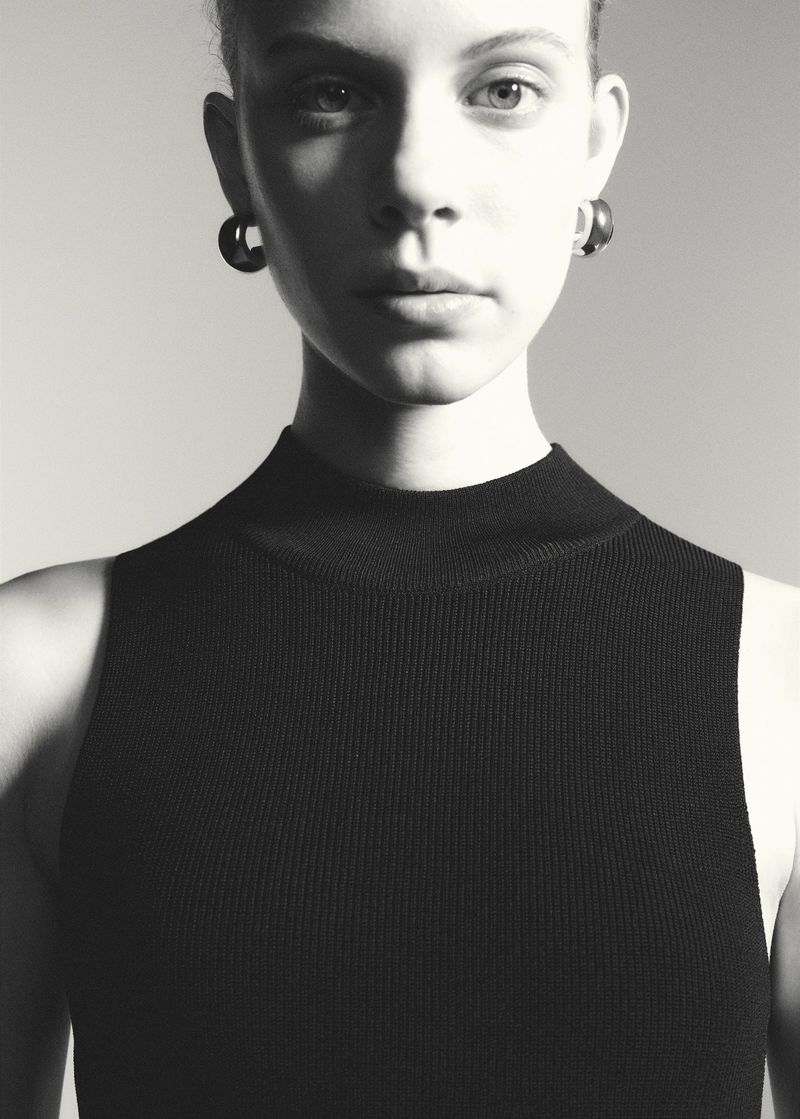 Monochrome portrait of a woman with dark earrings, wearing a black knit top, gazing forward in a studio setting with soft lighting.