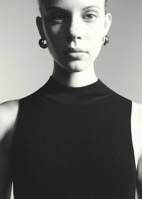 Monochrome portrait of a woman with dark earrings, wearing a black knit top, gazing forward in a studio setting with soft lighting.