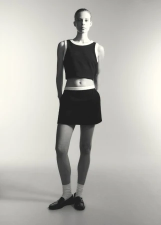 Model Anouk Smits posing in a black crop top with white trim and matching mini skirt for Mango's Formal 60's collection.