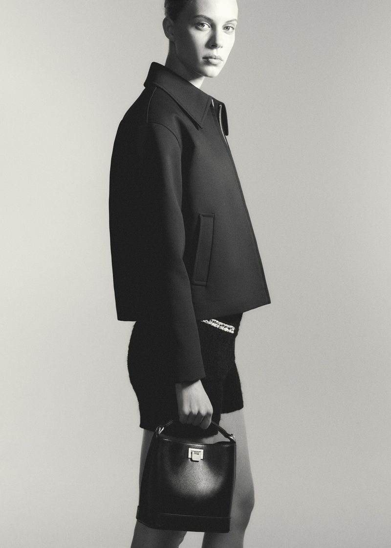 A black and white fashion shot features a female model in a dark jacket and shorts, holding a structured handbag against a neutral backdrop.