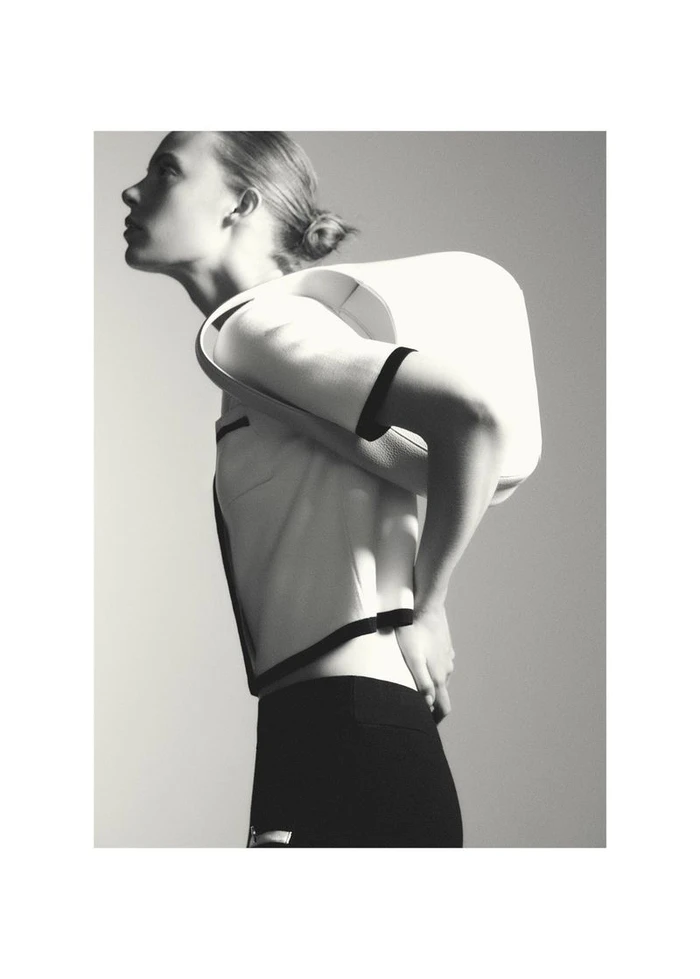 Model Anouk Smits in profile wearing a white top with black trim and a sculptural white piece against a neutral grey studio background.