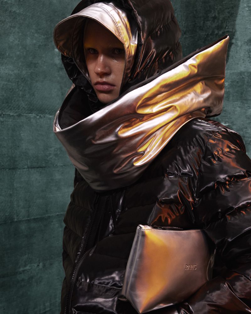 Close-up of a person wearing a shiny black puffer jacket with a metallic gold oversized hood and carrying a metallic gold clutch.