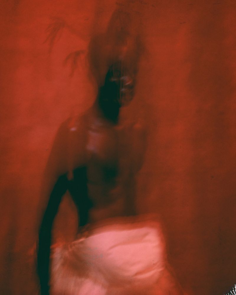 Blurry, dreamlike image featuring a figure against a red background; long exposure effects add an abstract feel.