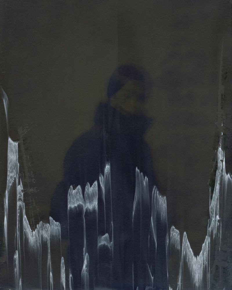 Abstract portrait of a person in a dark coat with blurred effects and a muted color palette, creating a somber and artistic mood.