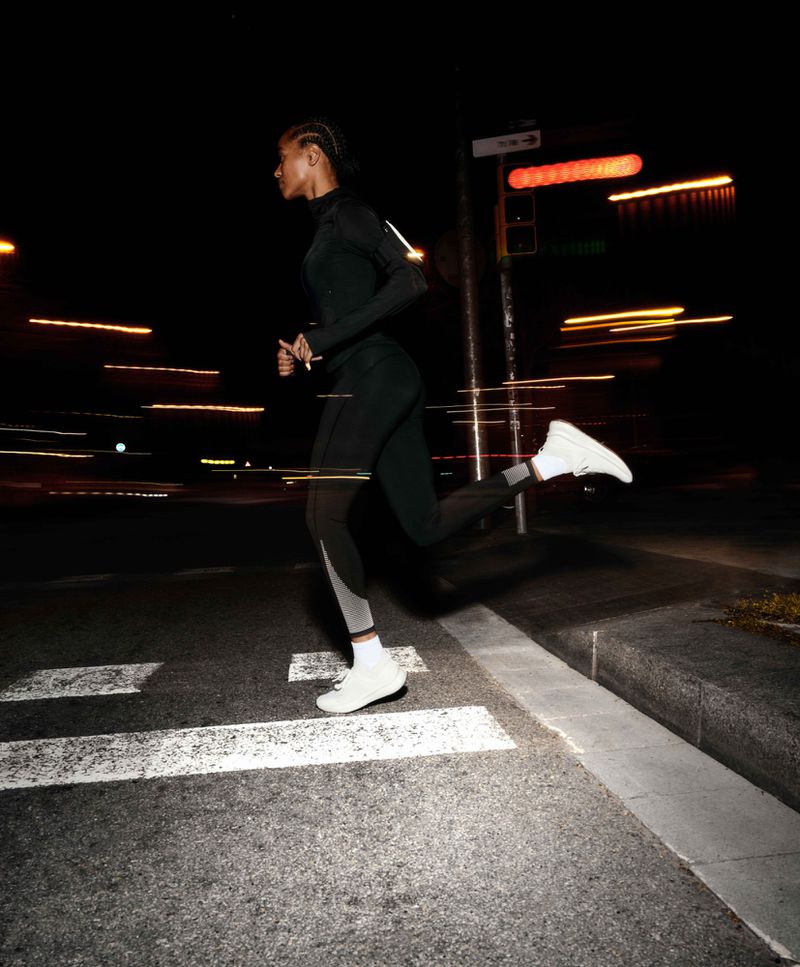 Athletic woman in fitness attire runs at night in an urban environment, featuring motion blur and dynamic street lighting, capturing energy and focus.