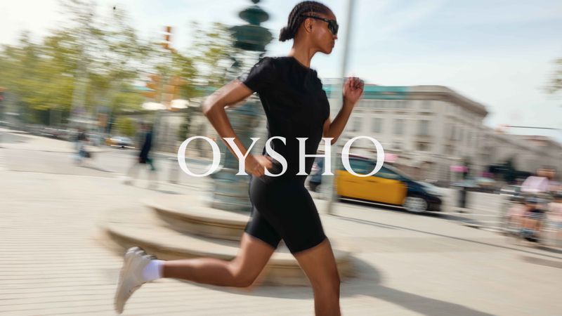 Woman in black athletic wear running in an urban setting with buildings and a yellow taxi, motion blur, and the Oysho logo.