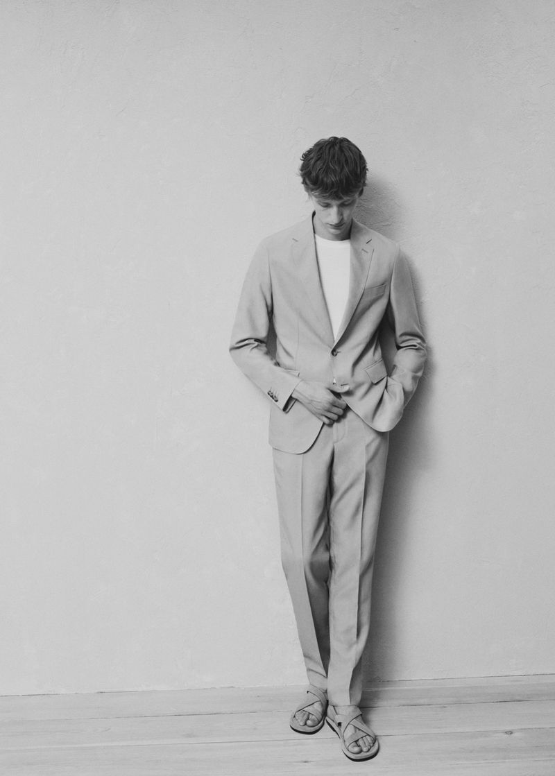 Model Nikita Stsjolokov posing in a tailored suit and strap sandals against a minimalist wall in monochrome.