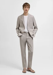 Model Nikita Stsjolokov poses in a light grey tailored suit, white t-shirt, and strappy sandals against a white seamless background.