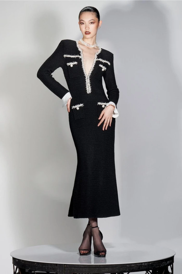 Model Li Linzi in a long black tweed dress with white trim and heels, standing on a circular podium against a studio backdrop.
