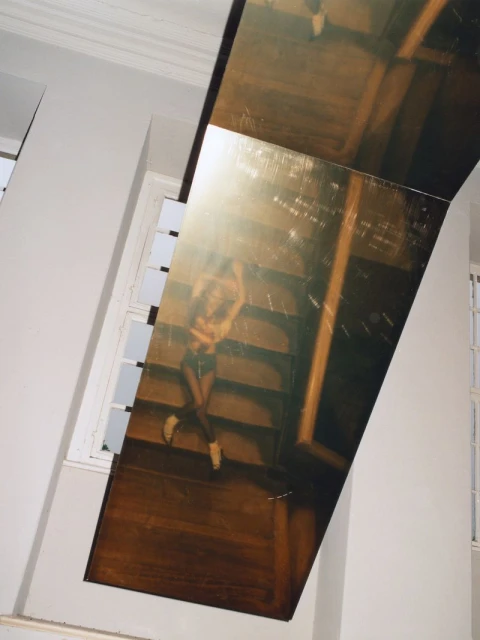 Abstract installation art featuring a print of a woman on stairs, mounted on a white wall with a window, in an indoor setting.