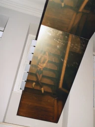 Model Gabbriette posing on wooden stairs seen through an angled reflective mirror panel in a bright room.