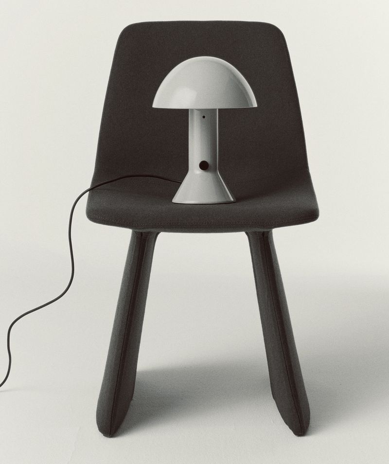 Indoor shot of a gray mushroom lamp on a modern dark gray chair, set against a clean white backdrop, creating a minimalist aesthetic.