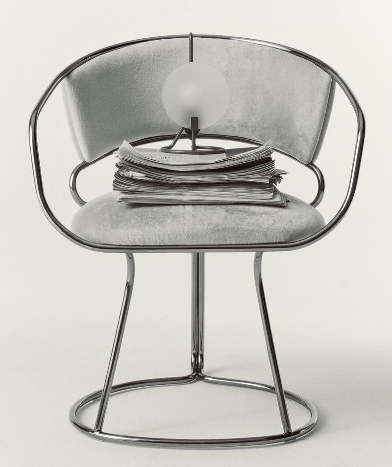 Chrome chair with grey cushions, a stack of newspapers, and a spherical lamp, set against a plain backdrop, creating a minimalist aesthetic.