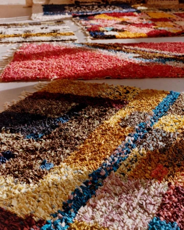Eye-level shot of colorful patterned rag rugs, featuring blue, brown, yellow, pink, and white tones, displayed indoors on a light surface.