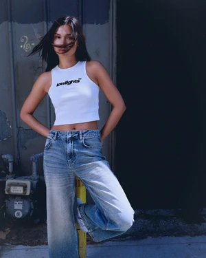 Model in white crop top and faded blue jeans leaning against a yellow post outdoors
