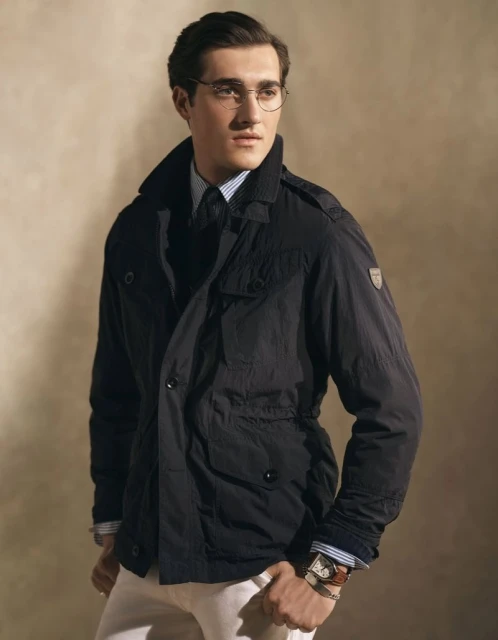Portrait of an adult male wearing glasses, a blue striped shirt, black tie, and a black jacket, posing in a studio with a neutral background.