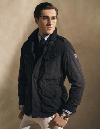 Portrait of an adult male wearing glasses, a blue striped shirt, black tie, and a black jacket, posing in a studio with a neutral background.