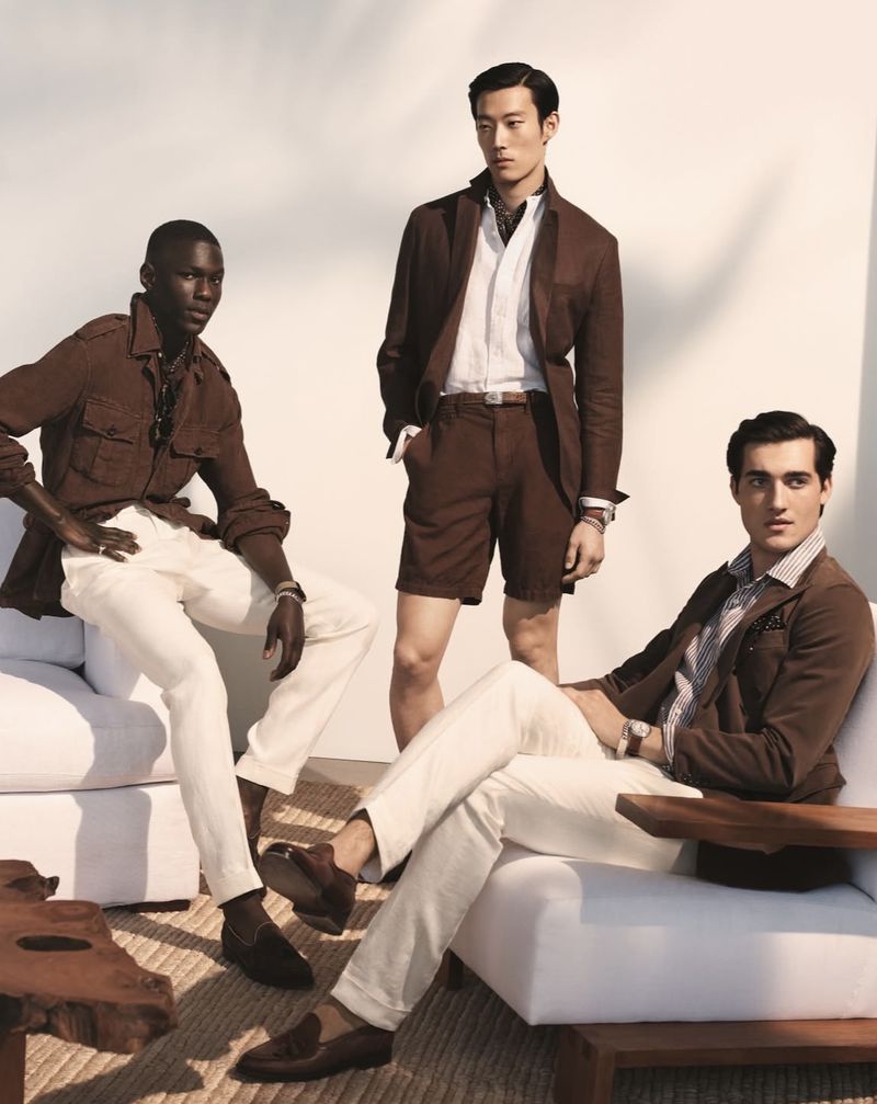 Three diverse male fashion models showcase brown and white summer outfits, sitting on white modern outdoor furniture against a bright background.