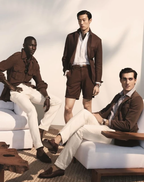 Three diverse male fashion models showcase brown and white summer outfits, sitting on white modern outdoor furniture against a bright background.