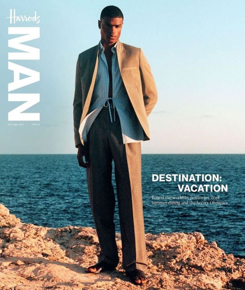 Harrods Man magazine cover featuring a male model in a suit, standing on a rocky outcrop with the ocean and sky in the background, bathed in sunlight.
