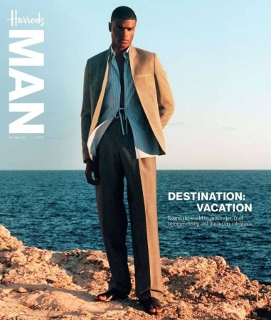 Harrods Man magazine cover featuring a male model in a suit, standing on a rocky outcrop with the ocean and sky in the background, bathed in sunlight.