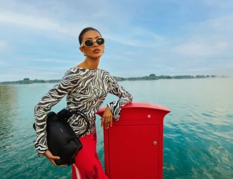 Model in zebra print top and sunglasses leaning on red box by the ocean for Bloomingdales ME campaign