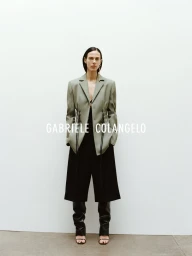 Model Aymeline Valade wearing a sage green blazer over a black outfit against a plain white background for Gabriele Colangelo.