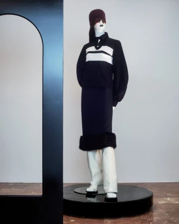 Fashion mannequin wearing a black and white striped shirt with black skirt and white boots, posing near a modern black arch.