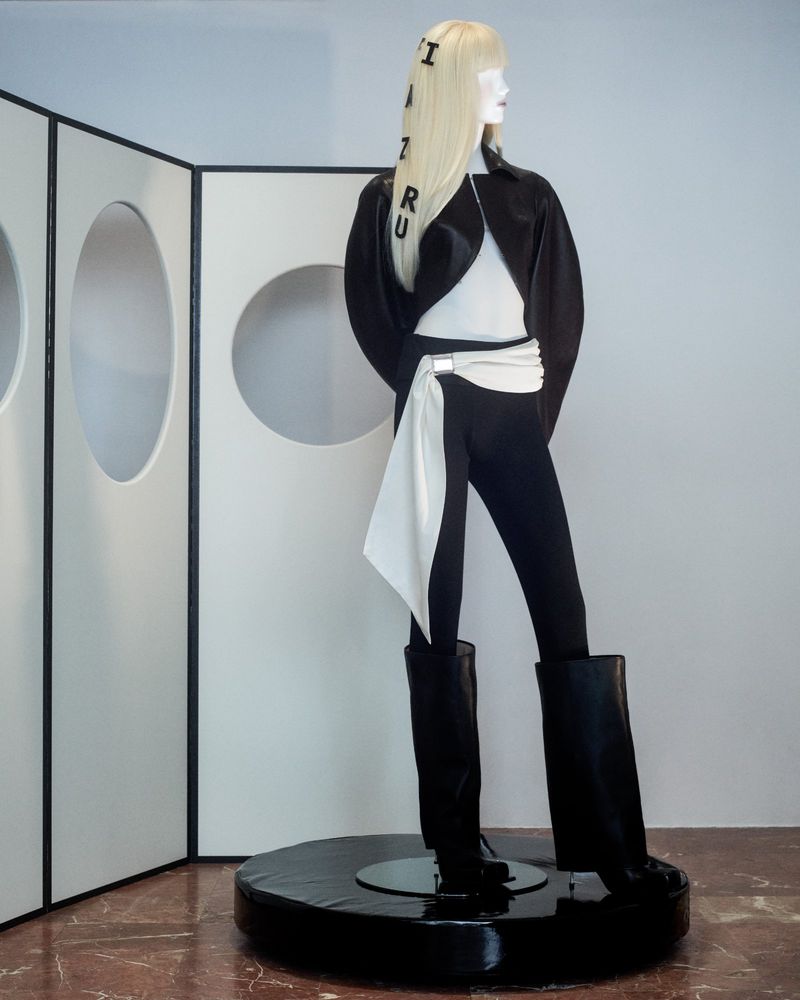 Mannequin displays black and white fashion in a minimalist studio setting with white walls and a geometric screen backdrop. 