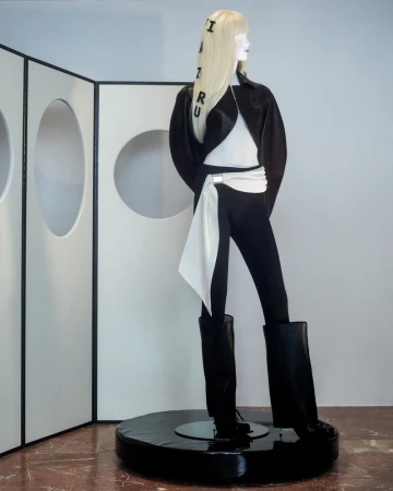 Mannequin displays black and white fashion in a minimalist studio setting with white walls and a geometric screen backdrop. 