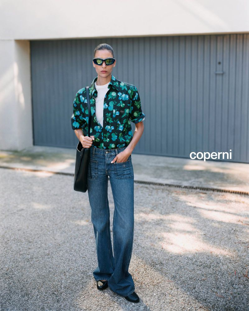 Model Nora Attal wearing futuristic sunglasses, printed shirt and denim jeans carrying a black handbag