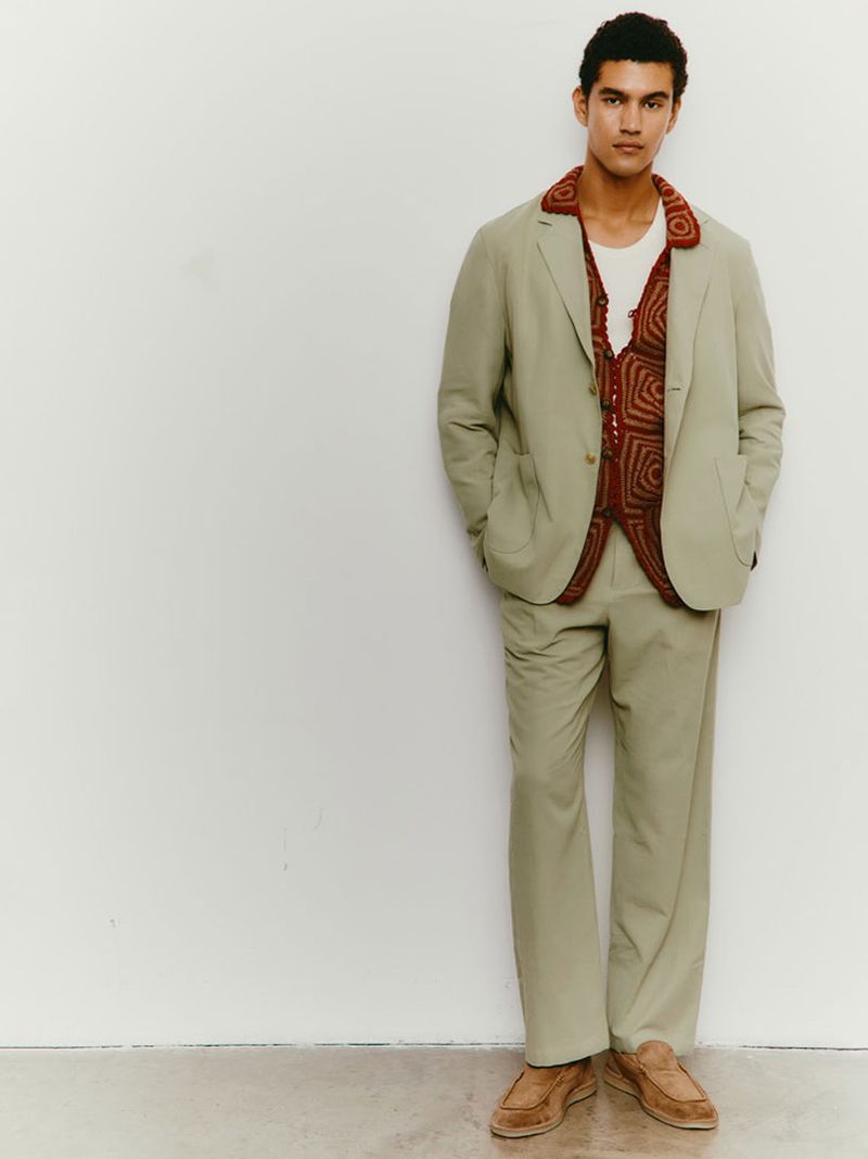 A stylish male model poses in a light green suit and brown loafers against a clean white backdrop for a fashion editorial shot.